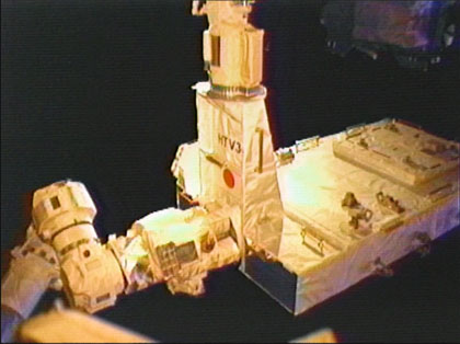画像：「きぼう」ロボットアーム（上）からISSのロボットアーム（左）に受け渡される曝露パレット