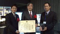 記念品と表彰状を手にする関係者（左から松村技術領域リーダ、桑尾氏（NEC）、土井主任開発員）