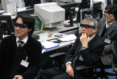 写真：実験運用管制室で実施の様子を見守るCIの川邊氏、PIの村山教授、CIの渡邊氏（左から）（3D用画面を見るため、専用メガネをかけている）