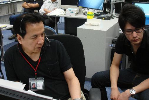 Prof. Tsukamoto (left) monitors the experiment proceeding from the User Operations Area (UOA) at the Tsukuba Space Center (TKSC) (Credit: JAXA)