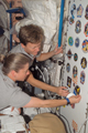 「ユニティ」（第1結合部）にて歴代スペースシャトルミッションのパッチのコレクションにSTS-120ミッションパッチを加えるパメラ・アン・メルロイ（手前）、ペギー・ウィットソン両宇宙飛行士（奥）（飛行13日目）