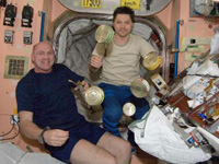 ESA astronaut AndrｸJ・Kuipers (left) and Russian cosmonaut Oleg Kononenko (right) with food items on the ISS in December 2011.  In the SOLO experiment, astronaut subjects undergo two different diet regimes to determine the physiological effects of sodium on the body. (Image: ESA)