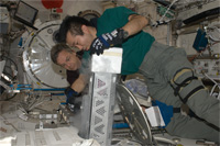 「きぼう」船内実験室で冷凍・冷蔵庫（MELFI）の作業を行う若田、サースク両宇宙飛行士